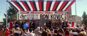 Movie still from “Born on the Fourth of July” (1989), directed by Oliver Stone – A group of people standing in front of an american flag; Wide shot, High angle