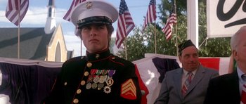 Movie still from “Born on the Fourth of July” (1989), directed by Oliver Stone – A man in a military uniform stands in front of american flags; Medium shot, Low angle
