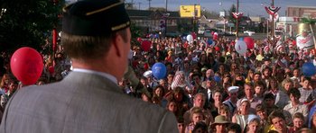 Movie still from “Born on the Fourth of July” (1989), directed by Oliver Stone – A large crowd of people gathered in the street for an event; Wide shot, High angle