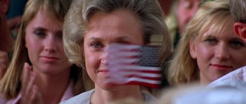 An older woman with blonde hair covering her face with an american flag