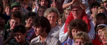 Movie still from “Born on the Fourth of July” (1989), directed by Oliver Stone – A group of people sitting in a crowd watching something; Close Up shot, Over the shoulder angle