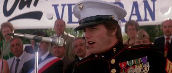 Movie still from “Born on the Fourth of July” (1989), directed by Oliver Stone – A man in a military uniform talking on a microphone; Close Up shot, Over the shoulder angle