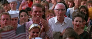 Movie still from “Born on the Fourth of July” (1989), directed by Oliver Stone – A group of men and women clapping at a sporting event; Close Up shot, Over the shoulder angle