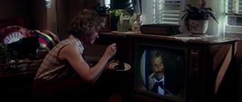 Movie still from “Born on the Fourth of July” (1989), directed by Oliver Stone – A man sitting in front of a tv eating a cake; Medium shot, Over the shoulder angle