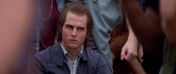 Movie still from “Born on the Fourth of July” (1989), directed by Oliver Stone – A man with a beard is sitting in front of a group of people; Close Up shot, Over the shoulder angle