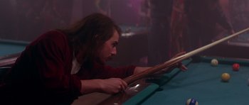 Movie still from “Born on the Fourth of July” (1989), directed by Oliver Stone – A man with long brown hair playing a game of billiards; Medium shot, Over the shoulder angle