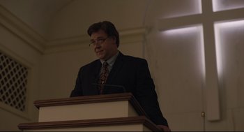 Movie still from “Boy Erased” (2018), directed by Joel Edgerton – A man standing at a podium in front of a microphone; Medium shot, Low angle