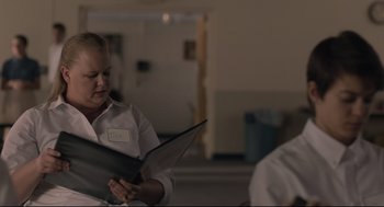 Movie still from “Boy Erased” (2018), directed by Joel Edgerton – A woman holding a binder in a room; Medium shot, Over the shoulder angle