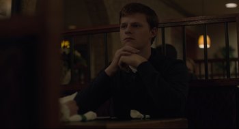 Movie still from “Boy Erased” (2018), directed by Joel Edgerton – A man sitting at a table with his hands folded on his chest; Medium shot, Over the shoulder angle