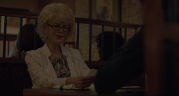 Movie still from “Boy Erased” (2018), directed by Joel Edgerton – An older woman sitting at a table looking at her cell phone; Medium shot, Over the shoulder angle