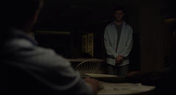 Movie still from “Boy Erased” (2018), directed by Joel Edgerton – A man standing next to a table in a dark room; Medium shot, Over the shoulder angle
