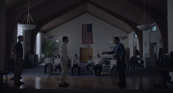 Movie still from “Boy Erased” (2018), directed by Joel Edgerton – Two men are standing in front of each other in front of a group of people; Wide shot, Low angle