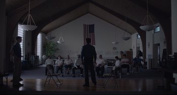 Movie still from “Boy Erased” (2018), directed by Joel Edgerton – A man standing in front of a group of people sitting in chairs; Wide shot, Low angle