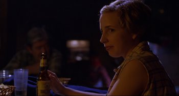 Movie still from “Boys Don't Cry” (1999), directed by Kimberly Peirce – A woman sitting at a table holding a bottle of beer; Close Up shot, Over the shoulder angle