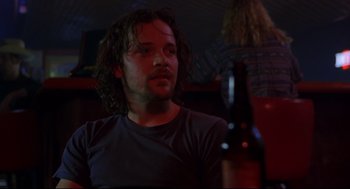 Movie still from “Boys Don't Cry” (1999), directed by Kimberly Peirce – A man with long hair is sitting in front of a bottle of beer; Close Up shot, Low angle