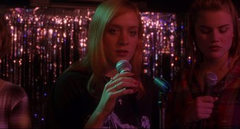 Movie still from “Boys Don't Cry” (1999), directed by Kimberly Peirce – A woman holding a microphone in front of a microphone stand; Close Up shot, Over the shoulder angle