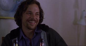 Movie still from “Boys Don't Cry” (1999), directed by Kimberly Peirce – A man with long dark hair sitting in front of a bottle of beer; Close Up shot, Over the shoulder angle