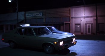 Movie still from “Boys Don't Cry” (1999), directed by Kimberly Peirce – An old car parked in front of a karate school at night; Wide shot, Low angle