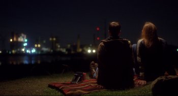 Movie still from “Boys Don't Cry” (1999), directed by Kimberly Peirce – A man sitting on a blanket in the grass at night; Wide shot, Over the shoulder angle