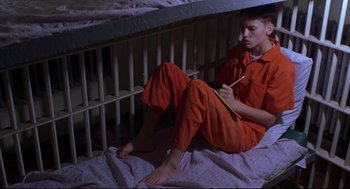 Movie still from “Boys Don't Cry” (1999), directed by Kimberly Peirce – A man in orange is sitting on a bed writing; Medium shot, High angle