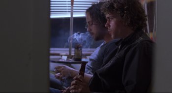 Movie still from “Boys Don't Cry” (1999), directed by Kimberly Peirce – Two men sitting in front of a window holding a cell phone; Medium shot, Low angle