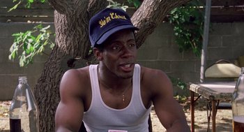 Movie still from “Boyz n the Hood” (1991), directed by John Singleton – A man wearing a hat sitting in front of a tree; Close Up shot, High angle