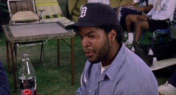 Movie still from “Boyz n the Hood” (1991), directed by John Singleton – A man in a baseball cap sitting in the grass; Close Up shot, Over the shoulder angle