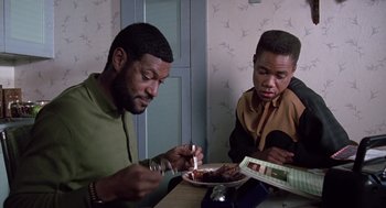 Movie still from “Boyz n the Hood” (1991), directed by John Singleton – Two men sitting at a table eating food; Medium shot, High angle
