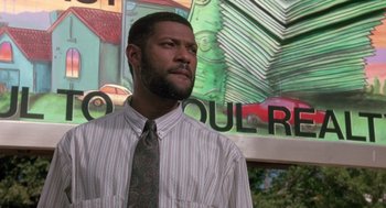Movie still from “Boyz n the Hood” (1991), directed by John Singleton – A man in a dress shirt and tie standing in front of a mural; Close Up shot, Low angle