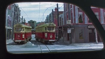 Movie still from “Dead Alive” (1992), directed by Peter Jackson – Two red and yellow trolleys on the tracks in a city; Wide shot, High angle