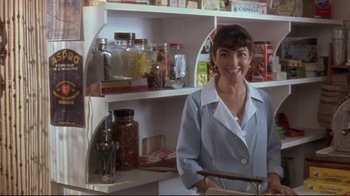 Movie still from “Dead Alive” (1992), directed by Peter Jackson – A woman standing in front of a shelf in a room; Medium shot, Low angle
