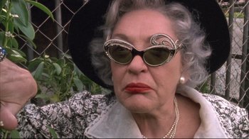 Movie still from “Dead Alive” (1992), directed by Peter Jackson – An older woman wearing sunglasses and a pearl necklace; Close Up shot, Low angle