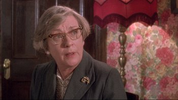 Movie still from “Dead Alive” (1992), directed by Peter Jackson – An older woman wearing glasses and a suit; Close Up shot, Over the shoulder angle