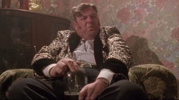 Movie still from “Dead Alive” (1992), directed by Peter Jackson – A man sitting on a couch with a glass of wine; Medium shot, Low angle