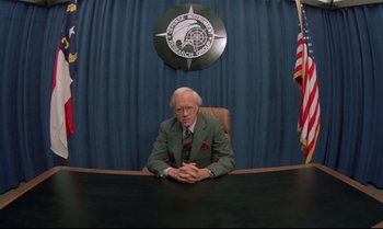 Movie still from “Brainstorm” (1983), directed by Douglas Trumbull – An older man sitting at a desk in front of a flag; Medium shot, Low angle