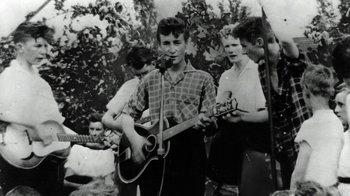 Movie still from “The Beatles: Eight Days a Week - The Touring Years” (2016), directed by Ron Howard – A group of young men playing guitars in a park; Medium shot, High angle