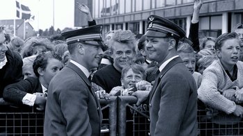 Movie still from “The Beatles: Eight Days a Week - The Touring Years” (2016), directed by Ron Howard – A couple of men standing next to each other on a street; Medium shot, Over the shoulder angle