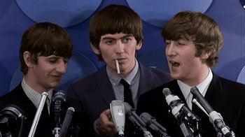 Movie still from “The Beatles: Eight Days a Week - The Touring Years” (2016), directed by Ron Howard – A group of men standing next to microphones in a room; Close Up shot, High angle