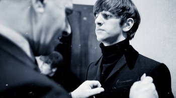 Movie still from “The Beatles: Eight Days a Week - The Touring Years” (2016), directed by Ron Howard – A young man in a black suit is looking at another young man; Close Up shot, Over the shoulder angle