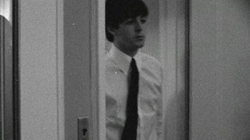 Movie still from “The Beatles: Eight Days a Week - The Touring Years” (2016), directed by Ron Howard – A man in a white dress shirt and black tie standing next to a door; Medium shot, Over the shoulder angle