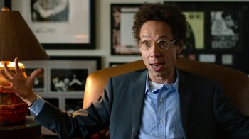 Movie still from “The Beatles: Eight Days a Week - The Touring Years” (2016), directed by Ron Howard – A man in a suit and glasses is sitting in an office chair; Close Up shot, Over the shoulder angle