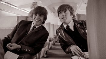 Movie still from “The Beatles: Eight Days a Week - The Touring Years” (2016), directed by Ron Howard – A couple of men sitting next to each other on a train; Medium shot, High angle