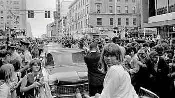 Movie still from “The Beatles: Eight Days a Week - The Touring Years” (2016), directed by Ron Howard – A black and white photo of a crowd of people on a street; Wide shot, High angle
