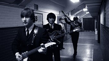 Movie still from “The Beatles: Eight Days a Week - The Touring Years” (2016), directed by Ron Howard – A black and white photo of a group of men playing guitar; Medium shot, High angle