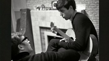 Movie still from “The Beatles: Eight Days a Week - The Touring Years” (2016), directed by Ron Howard – Two young men sitting in front of a fireplace; Medium shot, Over the shoulder angle