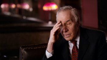 Movie still from “The Beatles: Eight Days a Week - The Touring Years” (2016), directed by Ron Howard – An older man wearing a suit and tie holding his hand to his forehead; Close Up shot, Over the shoulder angle