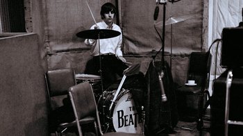 Movie still from “The Beatles: Eight Days a Week - The Touring Years” (2016), directed by Ron Howard – A man sitting on top of a drum set; Medium shot, High angle