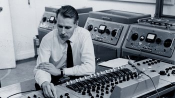 Movie still from “The Beatles: Eight Days a Week - The Touring Years” (2016), directed by Ron Howard – A man sitting at a table with a bunch of electronic equipment; Medium shot, High angle