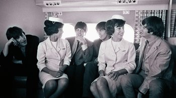 Movie still from “The Beatles: Eight Days a Week - The Touring Years” (2016), directed by Ron Howard – A group of people sitting next to each other on a couch; Medium shot, High angle
