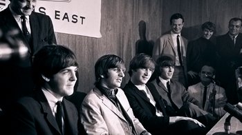 Movie still from “The Beatles: Eight Days a Week - The Touring Years” (2016), directed by Ron Howard – A group of men sitting next to each other in a room; Medium shot, High angle
